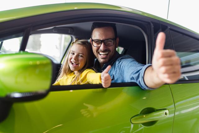 Vater und Kind in grünem Fahrzeug mit Daumen hoch aus Fenster.